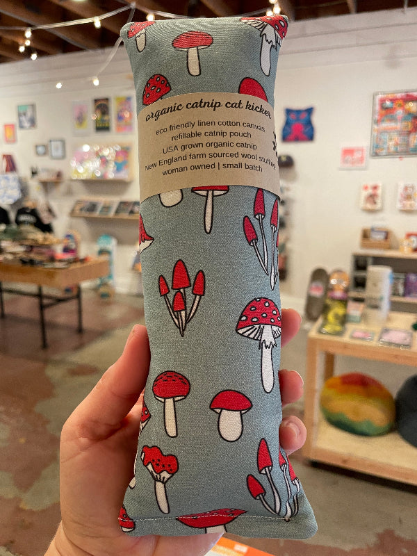 Catnip toy with mushroom pattern held in a hand, store interior in the background