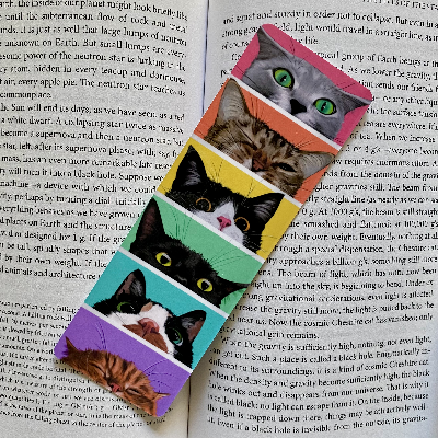 A colorful bookmark featuring a series of cat faces in a rainbow gradient, placed on an open book.